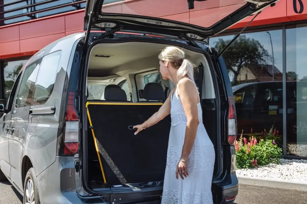 Coffre ouvert du VW Caddy ou FORD Tourneo Connect TPMR avec une femme qui ouvre la rampe