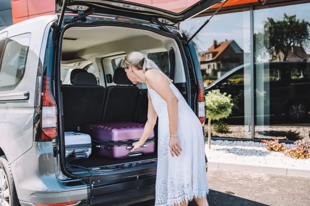 Coffre ouvert du VW Caddy ou FORD Tourneo Connect TPMR avec une femme qui retire des valises